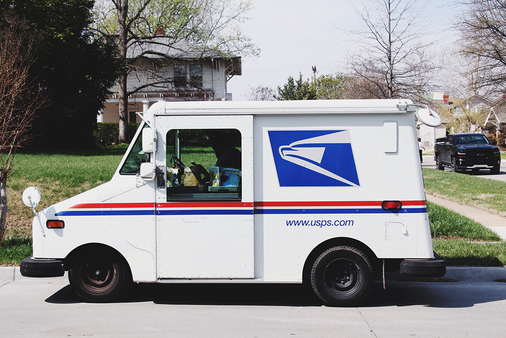 Image of a USPS truck and driver outside of a home